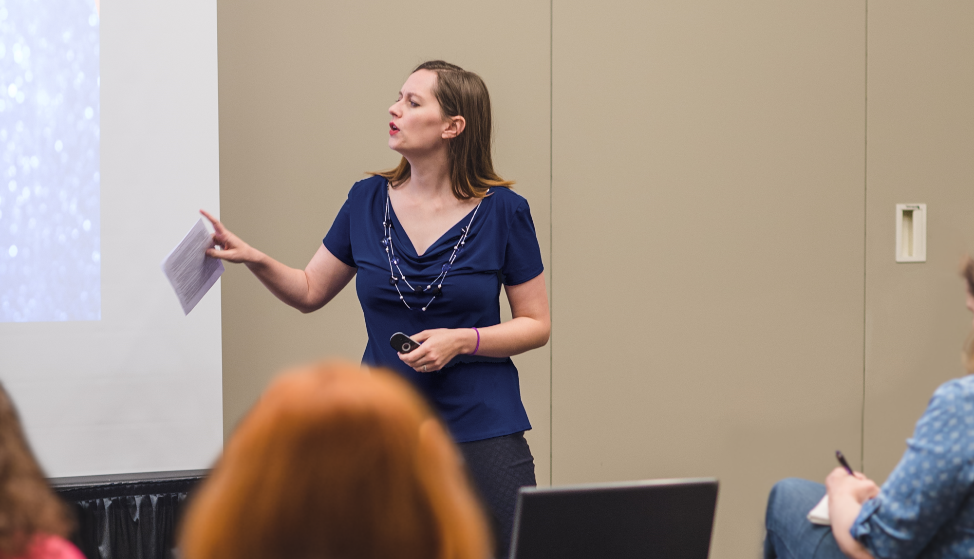 Jordan McCollum, a white woman in her thirties with long brown hair, wearing a navy shirt, teaching in a conference classroom. Photo by Erin Summerill